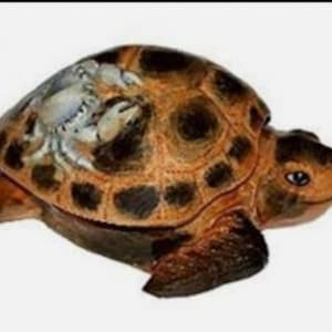 Könnte beinhalten: Dekorative Schildkrötenfigur mit braun-schwarz gemustertem Panzer. Der Kopf und die Gliedmaßen der Schildkröte sind hellbraun. Der Panzer hat ein einzigartiges Design mit dunklen Flecken und einem helleren Fleck.