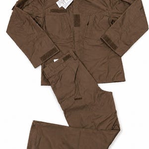 Puede incluir: Un conjunto de uniforme táctico de color marrón sólido que consta de una chaqueta de manga larga y pantalones a juego. La chaqueta presenta un cuello alto, parches de velcro en el pecho y las mangas, y una etiqueta blanca en el cuello.