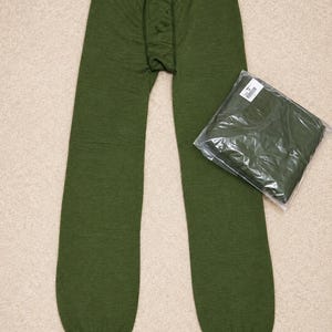 Könnte beinhalten: Eine olivgrüne Thermounterhose mit elastischem Bund und gerippten Bündchen an den Knöcheln. Neben dem entfalteten Kleidungsstück liegt ein zweites Paar identischer olivgrüner Thermounterhosen, das in einer durchsichtigen Plastiktüte verpackt ist.