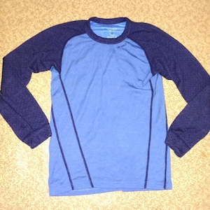 Puede incluir: Una camiseta azul de manga larga con un diseño de manga raglan azul marino. La camiseta tiene cuello redondo y la palabra "REVOLO" está impresa en la parte delantera.