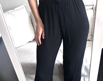 May include: Black cropped pants with a drawstring waist. The pants are made of a lightweight fabric and have a relaxed fit. The model is wearing a black bra top.