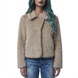 Può includere: Una giacca in pelliccia sintetica color beige con colletto ampio e maniche lunghe, caratterizzata da una finitura morbida e testurizzata. La giacca è indossata sopra un paio di jeans in denim blu, creando un look casual. L'orlo è dritto.