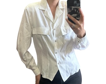 May include: White button-down shirt with two chest pockets and decorative embroidery on the collar and cuffs. The shirt has a tailored fit and is made of a textured fabric. The shirt is buttoned up and has a classic collar.