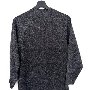 May include: A black and silver speckled jumper with long sleeves and a mock neck, suspended on a black hanger against a white backdrop. The fabric of the jumper has a textured appearance.