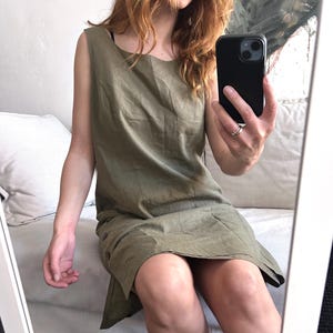 May include: Olive green sleeveless dress with a scoop neckline and button details. The dress appears to be made of linen or a similar lightweight fabric. The hemline is slightly asymmetrical.