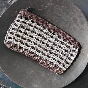 May include: A rectangular pouch constructed from dark brown crocheted cord and silver-colored aluminum soda can tabs. The pouch features a zipper closure along the top edge, with the metallic tabs arranged in a grid pattern across the front surface.