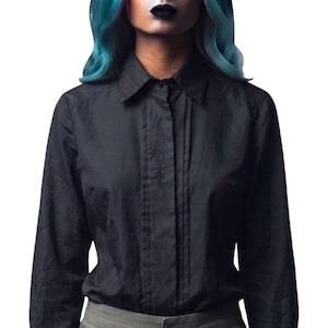 May include: A black long-sleeved button-down shirt featuring a pointed collar and a vertical placket with subtle tonal embroidery. The shirt has a structured fit with vertical pleats running down the front, providing a clean and uniform appearance.