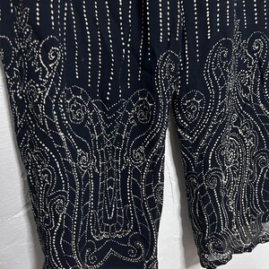 Könnte beinhalten: Eine dunkel marineblaue Hose mit einem cremefarbenen Punktemuster. Das Design umfasst vertikale punktierte Linien im oberen Bereich und ein dichtes, komplexes, von Paisley inspiriertes Punktemuster am unteren Teil der Hosenbeine.