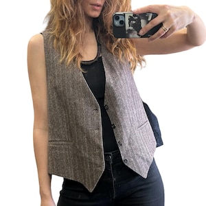 Puede incluir: Un chaleco marrón con diseño de espiga, cuello en V y tres botones. El chaleco tiene dos bolsillos delanteros y un corte entallado. La tela tiene una textura sutil y un estilo clásico.