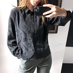 Peut inclure: Chemise noire boutonnée avec un motif géométrique subtil. La chemise à manches longues a un col et est faite d'une matière soyeuse. La chemise fait partie d'une collection de vêtements.