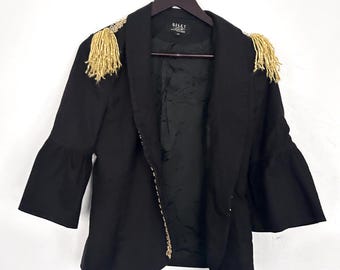 Pode incluir: Blazer preto com detalhes dourados nos ombros. O blazer tem gola e mangas compridas. A etiqueta "Riley Rose" é visível na frente.