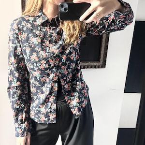 May include: A navy blue floral shirt with red, pink, and green flowers. The long-sleeved shirt is worn with black trousers. The image is reflected in a mirror.