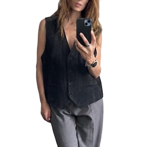 Può includere: Un gilet in camoscio grigio antracite scuro con scollo a V, chiusura frontale con quattro bottoni abbinati e due tasche orizzontali a filetto in vita. Il capo senza maniche presenta un taglio sartoriale e un orlo anteriore a punta.