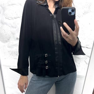 Peut inclure: Une chemise noire à manches longues avec une fermeture éclair et une bordure en satin. La chemise a un détail de boucle décoratif sur le devant.