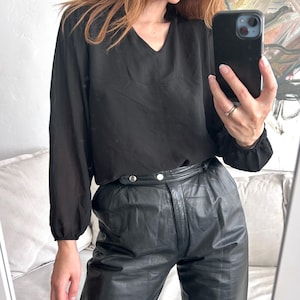 Op de afbeelding: Een zwarte blouse met lange mouwen, een v-hals en een zwarte leren broek.
