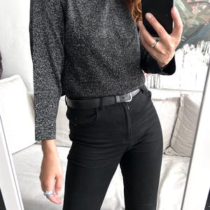 May include: A long-sleeved, dark grey, sparkly jumper paired with black jeans and a black belt. The outfit is reflected in a mirror, showcasing a casual, everyday style.