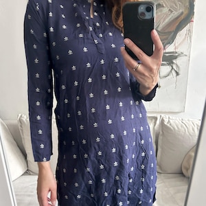 May include: Navy blue tunic with a mandarin collar and long sleeves. The tunic is adorned with a repeating pattern of small, white floral motifs. The fabric appears to be lightweight and slightly textured, with a relaxed fit.