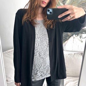 Peut inclure: Un cardigan noir à manches longues avec un chemisier en dentelle en dessous. Le cardigan est ample et ouvert sur le devant.