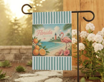 Puede incluir: Una bandera de jardín rectangular con un borde a rayas de color verde azulado y blanco en la parte superior e inferior. La ilustración central muestra una escena de playa con un flamenco rosa, un faro, palmeras, naranjas y el texto Florida.