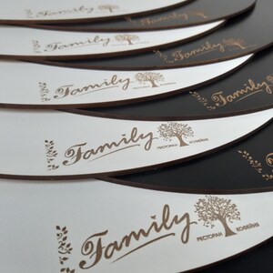 May include: A stack of white round coasters with a brown "Family" logo and a tree design. The coasters have a black backing.