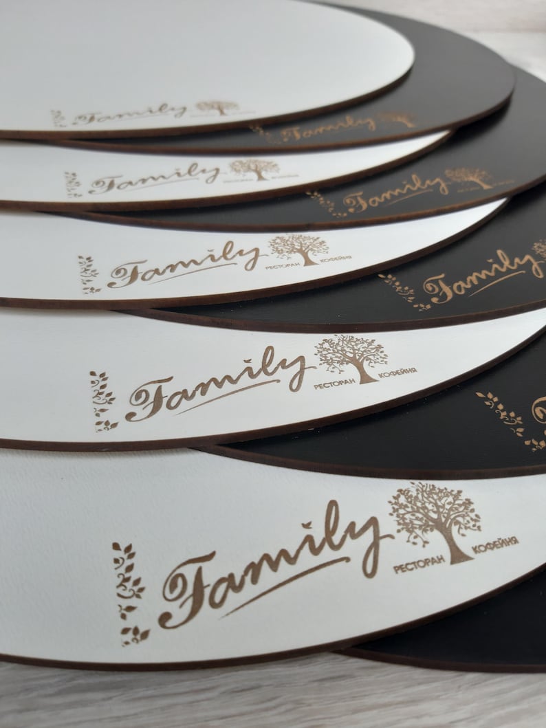 May include: A stack of white round coasters with a brown "Family" logo and a tree design. The coasters have a black backing.