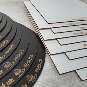 May include: A stack of black round cake boards with the text "095 016 27 39" and a cupcake graphic printed on each board. The boards are stacked on top of each other, with the largest board at the bottom and the smallest board at the top. The boards are all the same size, but they are stacked in a way that makes them look like they are getting smaller as they go up. The boards are all black, and they have a smooth, glossy finish.