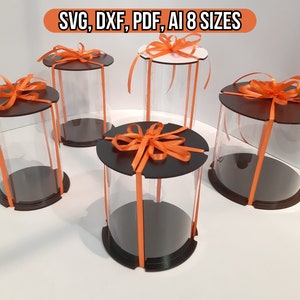 May include: Five clear plastic cylinder boxes with black bases and orange ribbon bows. The boxes are arranged on a white surface. The text "SVG, DXF, PDF, AI 8 SIZES" is visible at the top of the image.