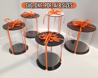 May include: Five clear plastic cylinder boxes with black bases and orange ribbon bows. The boxes are arranged on a white surface. The text "SVG, DXF, PDF, AI 8 SIZES" is visible at the top of the image.