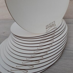 May include: A stack of 15 white round cake boards with a brown swirl design. The top board has the phone number 099 097 19 56 and the text "ANDRIANA-T" printed on it.