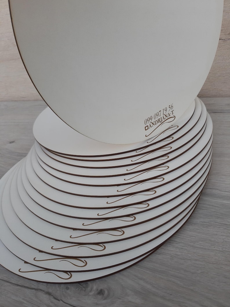 May include: A stack of 15 white round cake boards with a brown swirl design. The top board has the phone number 099 097 19 56 and the text "ANDRIANA-T" printed on it.