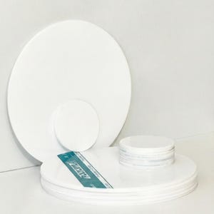 May include: A collection of white, circular objects of varying sizes. Several flat discs are stacked, with a larger disc behind them. A blue and white label with text is visible.