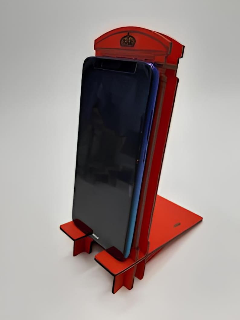 May include: Red phone booth shaped phone stand with a black smartphone in the stand.