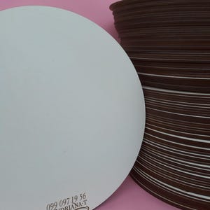 May include: A stack of round, brown cardboard cake boards with a single white cake board on top. The white cake board has the text "099 097 19 56 ANDRIANA-T" printed on it.