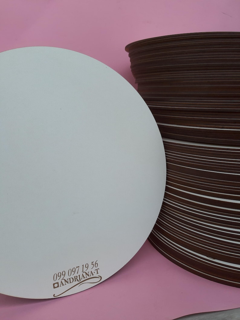 May include: A stack of round, brown cardboard cake boards with a single white cake board on top. The white cake board has the text "099 097 19 56 ANDRIANA-T" printed on it.