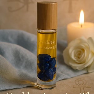 May include: A clear glass roller bottle with a wooden cap, filled with yellow oil and blue lapis lazuli stones. The bottle is labeled "Goddess Intention Oil." A lit candle and a white rose are in the background.