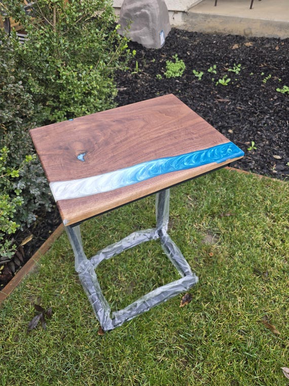 A live-edge walnut C-table with an electric-blue epoxy river vein — slides under the sofa and doubles as a laptop stand with serious 'how is that real wood?' energy.