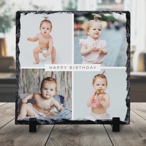 May include: A black slate photo frame displaying four images of a baby, with the text "HAPPY BIRTHDAY" in white. The frame is supported by two black stands and rests on a wooden surface.