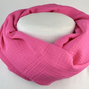 Könnte beinhalten: Ein rosa Baumwollschal mit strukturierter Oberfläche. Der Schal ist gefaltet und auf einer weißen Puppe ausgestellt.
