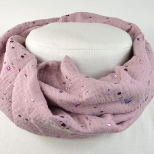 Könnte beinhalten: Staubrosa Infinity-Schal mit schillernden Pailletten-Akzenten. Der weiche, strukturierte Stoff ist um eine weiße Form drapiert und zeigt das kreisförmige Design des Schals. Dieses Accessoire verleiht jedem Outfit einen Hauch von Glanz.