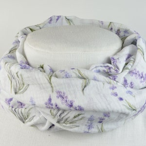 Könnte beinhalten: Weißer Baumwollschal mit einem Lavendel-Blumenmuster. Der Schal ist gefaltet und auf einer weißen Schaufensterpuppe ausgestellt.