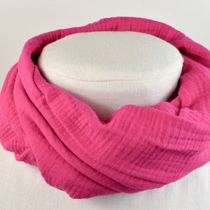 Könnte beinhalten: Ein rosa Baumwollschal mit strukturierter Oberfläche. Der Schal ist gefaltet und auf einer weißen Puppe ausgestellt.