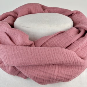 Könnte beinhalten: Ein weicher, rosa Schal aus Baumwolle mit einer strukturierten, waffelartigen Webart. Der Schal ist gefaltet und über eine weiße Schaufensterpuppe gelegt.