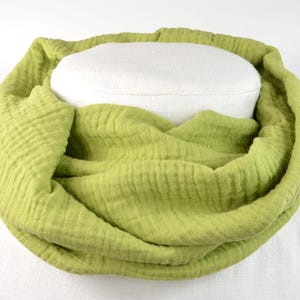 Könnte beinhalten: Ein hellgrüner Loop-Schal aus weichem, strukturiertem Stoff. Der Schal ist um eine weiße Form drapiert, wodurch sein kreisförmiges Design hervorgehoben wird. Der Stoff wirkt leicht und atmungsaktiv, passend für verschiedene Jahreszeiten.