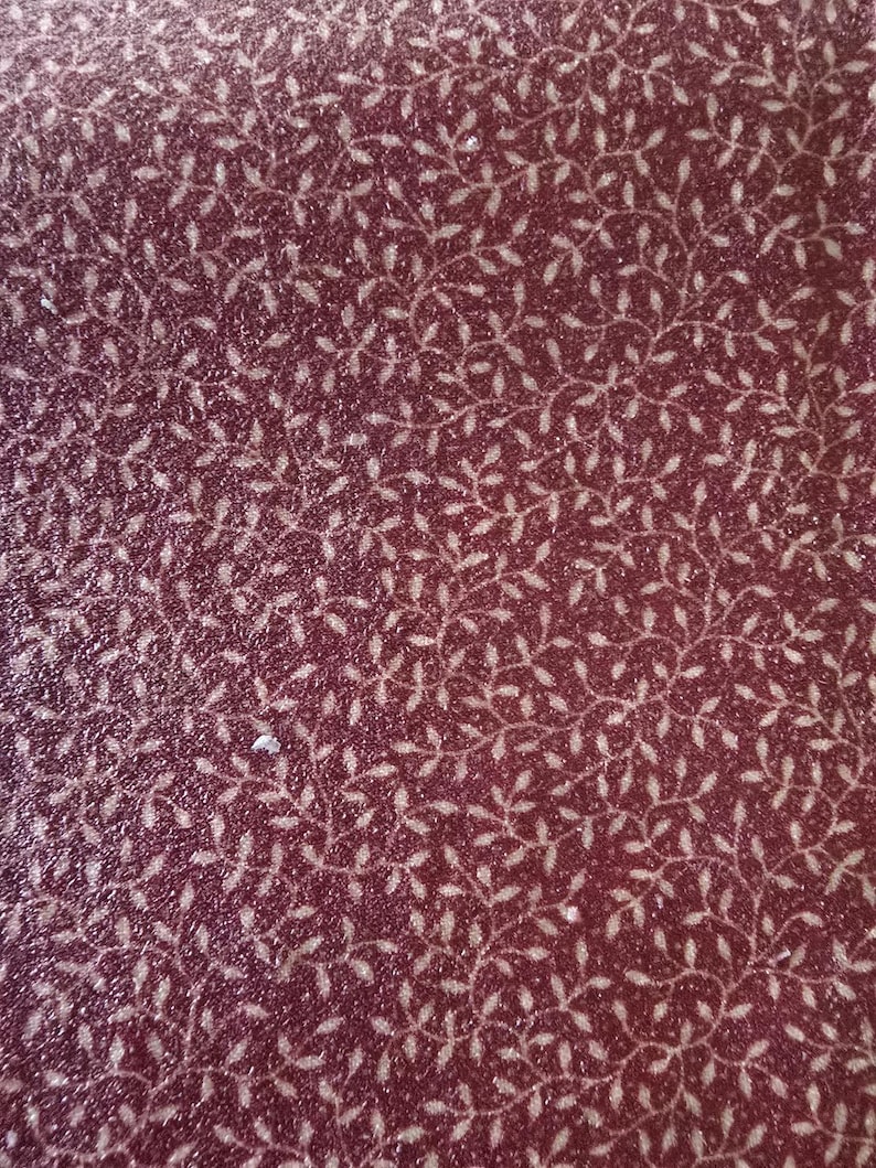 May include: Close-up of a burgundy fabric with a repeating pattern of delicate, white, leaf-like designs. The fabric has a subtle, textured appearance, with a slight sheen. The overall effect is one of understated elegance and natural motifs.
