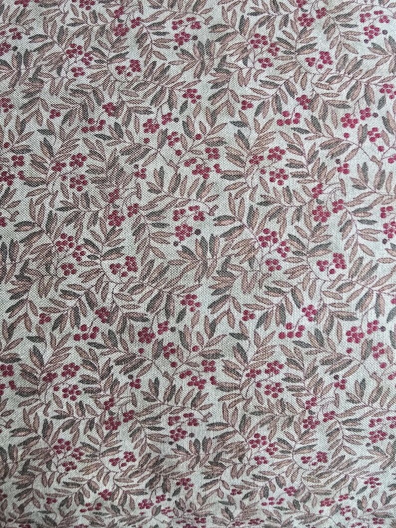 May include: Close-up of a fabric with a repeating pattern of leaves and berries. The leaves are a muted brown, and the berries are a deep red. The background is a light beige color, creating a natural, rustic aesthetic.