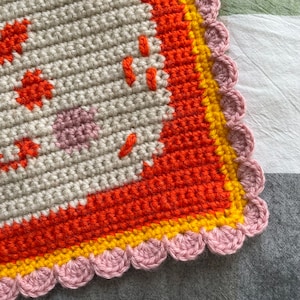 K&ouml;nnte beinhalten: Nahaufnahme einer geh&auml;kelten Decke mit einem rosa, gelben und orangenen Rand. Die Decke ist mit verschiedenen Maschen gearbeitet und hat eine strukturierte Oberfl&auml;che.