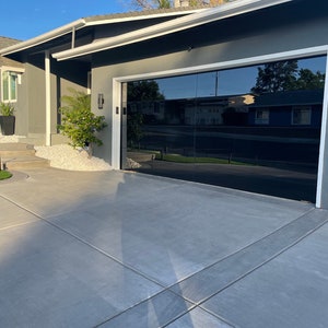 May include: A modern home with a black glass garage door. The door is reflective and shows the surrounding neighborhood. The home has a gray exterior with white trim.