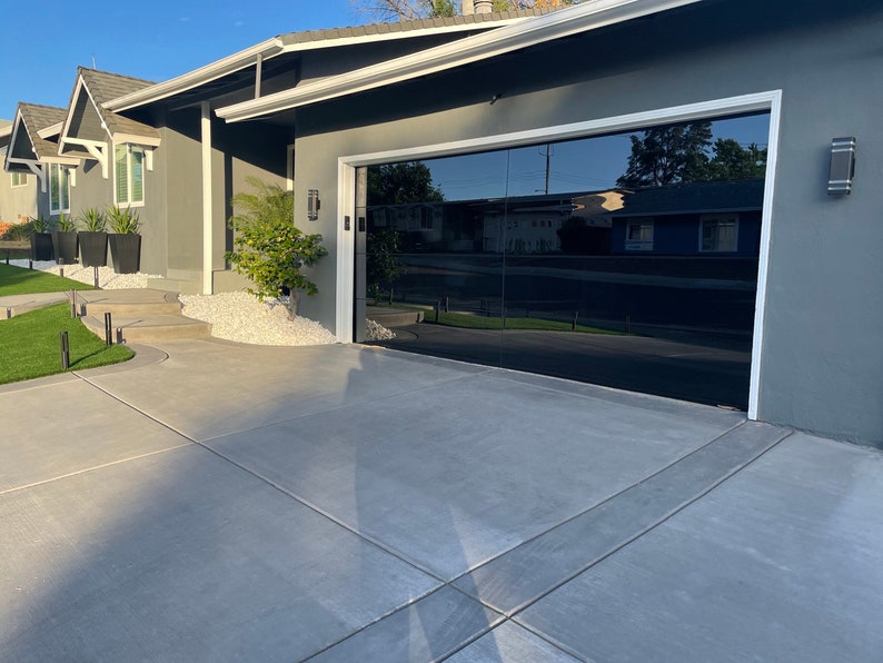 May include: A modern home with a black glass garage door. The door is reflective and shows the surrounding neighborhood. The home has a gray exterior with white trim.