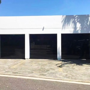 May include: Three black garage doors with a white wall behind them. The doors are closed and have a smooth, glossy finish.