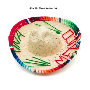 Op de afbeelding: Een traditionele Mexicaanse sombrero met een strooien basis en een kleurrijk geborduurd band. Het band heeft rode, oranje, gele, groene, blauwe en zwarte strepen. De hoed is versierd met groene borduurwerk en het woord "Mexico" in rood borduurwerk.